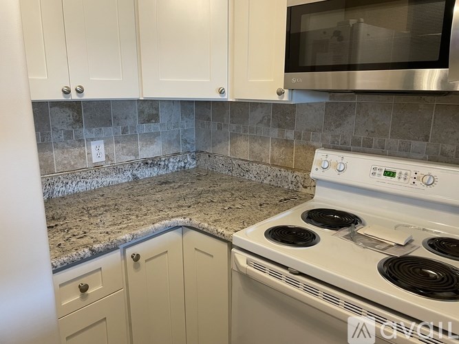 A kitchen with a white stove top oven and white cabinets.