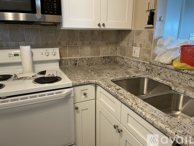 A kitchen with a white stove, white cabinets, and a granite countertop.
