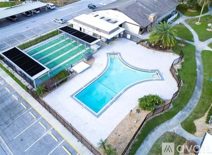 An aerial view of a swimming pool and a building with a parking lot in front.