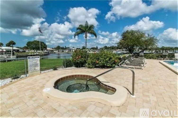 A hot tub sits in the middle of a patio with a pool and palm tree in the background.