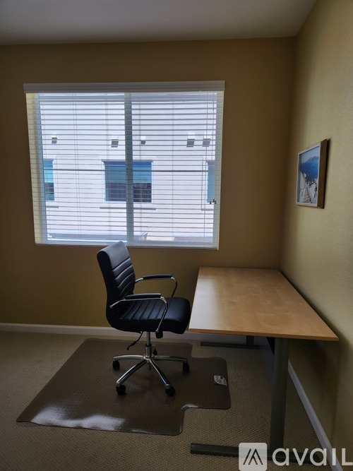 A black office chair is in front of a window with blinds.