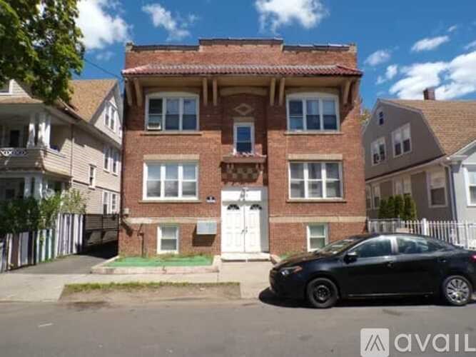 A black car is parked in front of a two-story brick house.