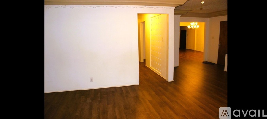 A room with wooden floors and a white wall with a doorway leading to another room.