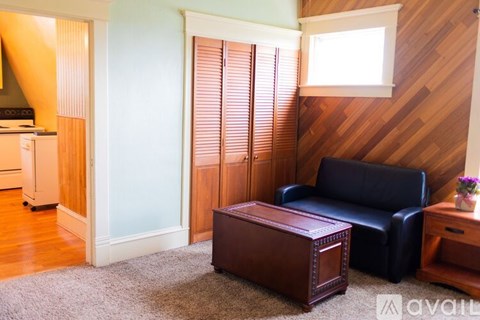 A living room with a black leather couch, a wooden coffee table, and a window with blinds.
