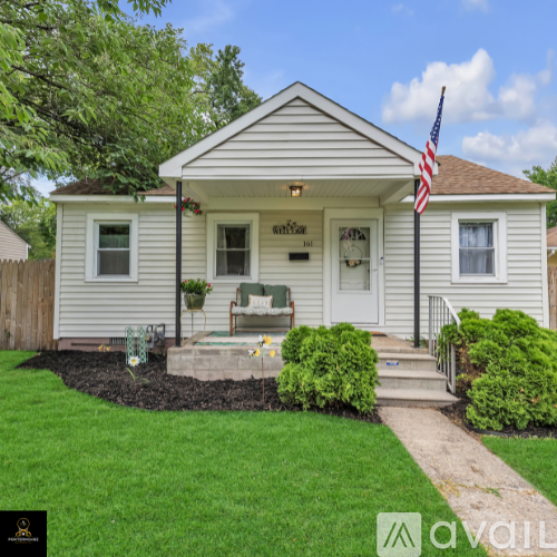 A small white house with a porch and an American flag on the front.
