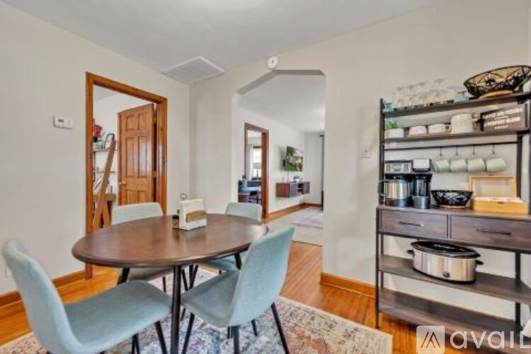 A kitchen with a table and chairs in the foreground and a shelf with pots and pans on it.
