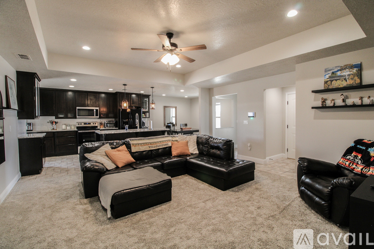 A spacious living room with a black couch and a kitchen area in the background.