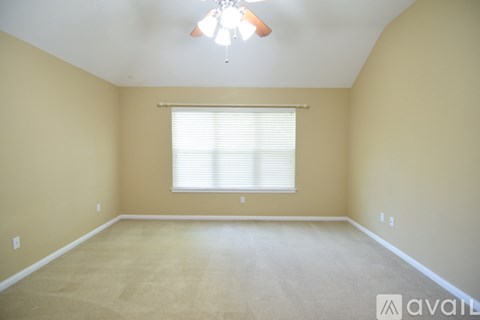 A room with beige walls and carpeting, a window with blinds, and a chandelier hanging from the ceiling.