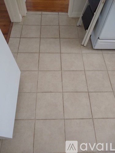 A kitchen with a white fridge and beige tiled floor.