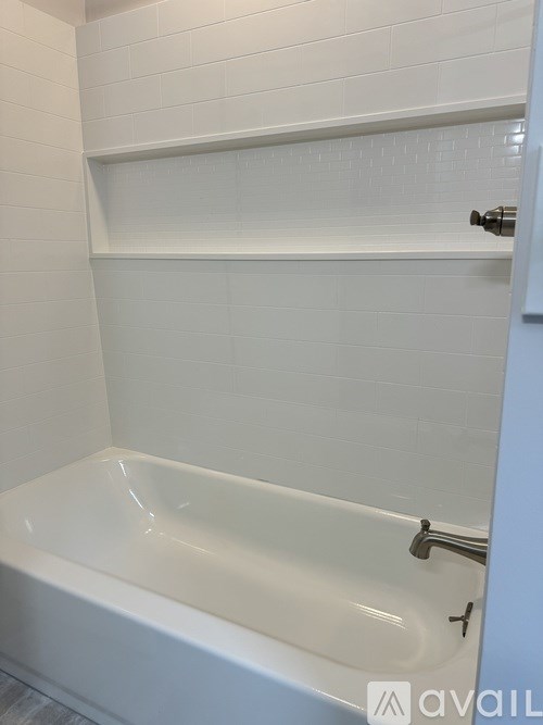 A white bathroom with a bathtub and a shelf above it.