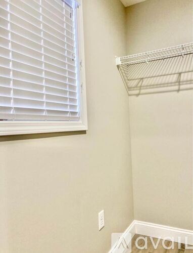 A white shelf is mounted on a wall next to a window with white blinds.