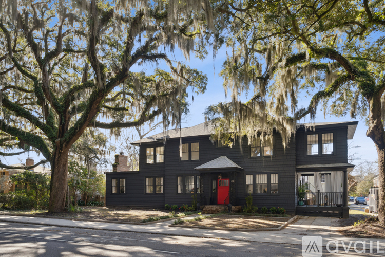A large house with a red door is surrounded by trees with Spanish moss hanging from them.
