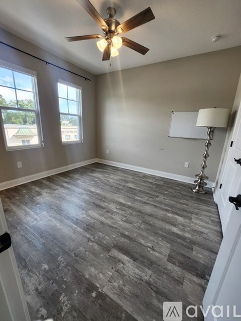 A room with a ceiling fan and grey wood flooring.