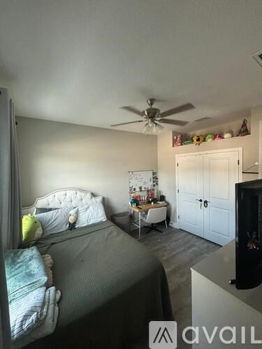 A bedroom with a bed, a desk, and a ceiling fan.