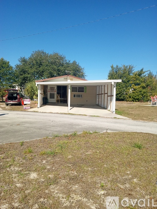 A small white building with a red vehicle parked in front.