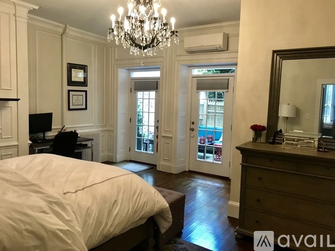 A bedroom with a large bed, a chandelier, and a dresser with a mirror.
