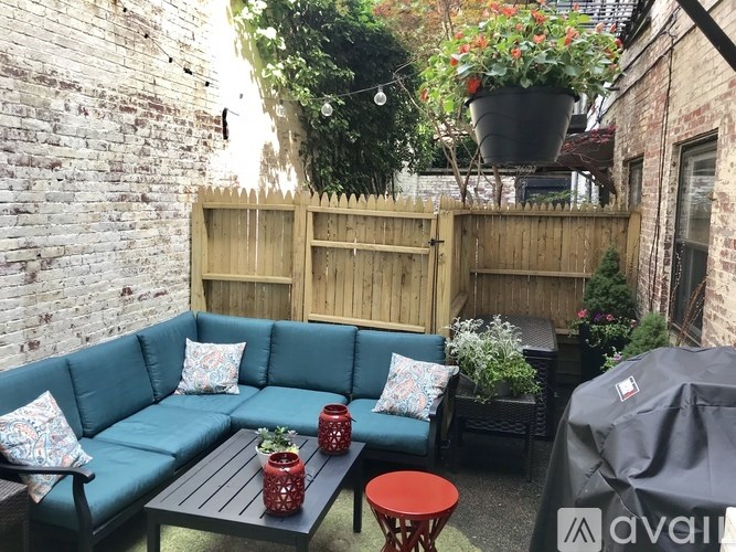 A patio with a blue couch, a table with a vase, and a fence.