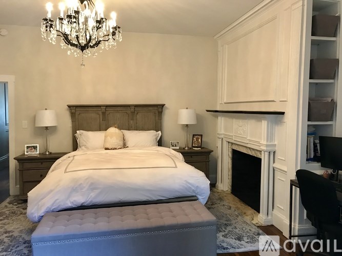 A large bed with a white comforter and two pillows is in the center of a room with a chandelier and a fireplace.