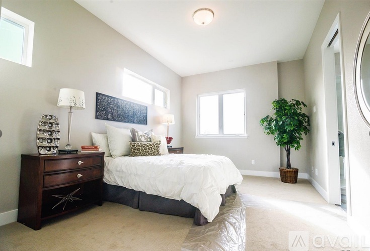 A bedroom with a bed, nightstand, and a plant.
