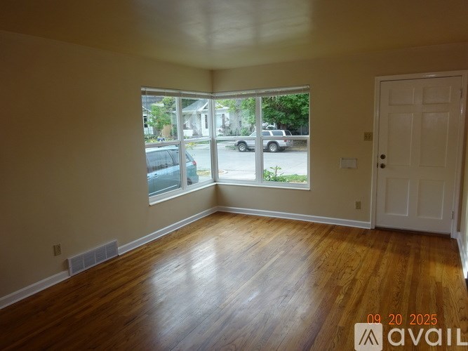 A room with wooden floors and a large window overlooking a street.