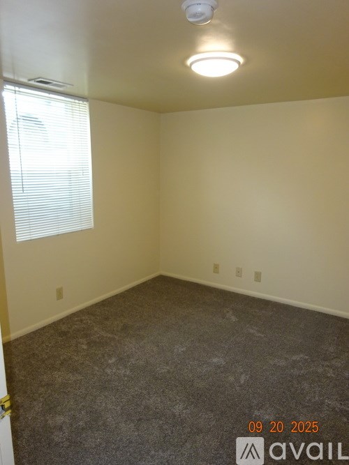 A room with a smoke detector on the ceiling and a window with blinds.