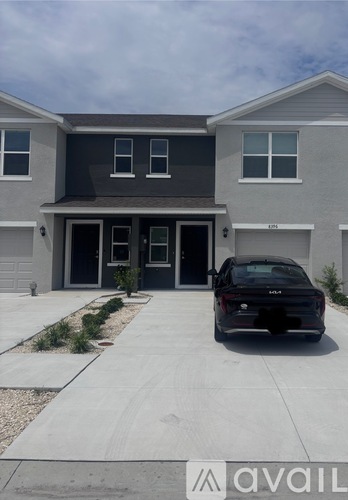A black car is parked in front of a grey house.