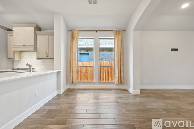 A spacious room with wooden flooring and a window with curtains.