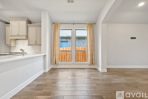 A spacious room with wooden flooring and a window with curtains.
