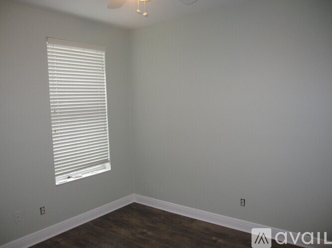 A room with a window covered by white blinds and wooden flooring.