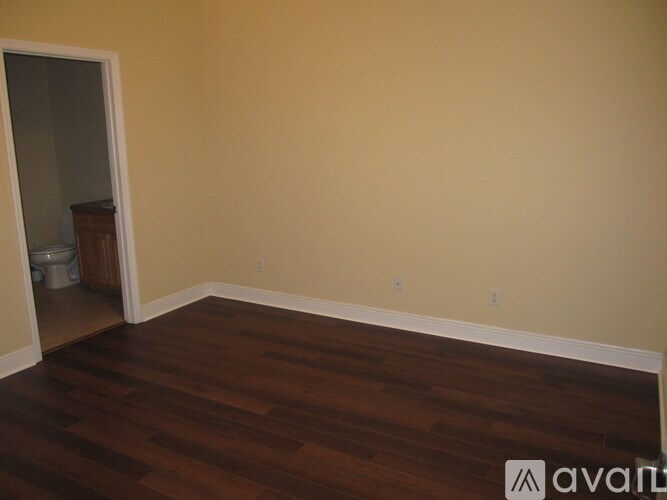 A room with wooden floors and a doorway leading to a bathroom.