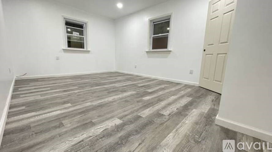 A room with wooden flooring and two windows.