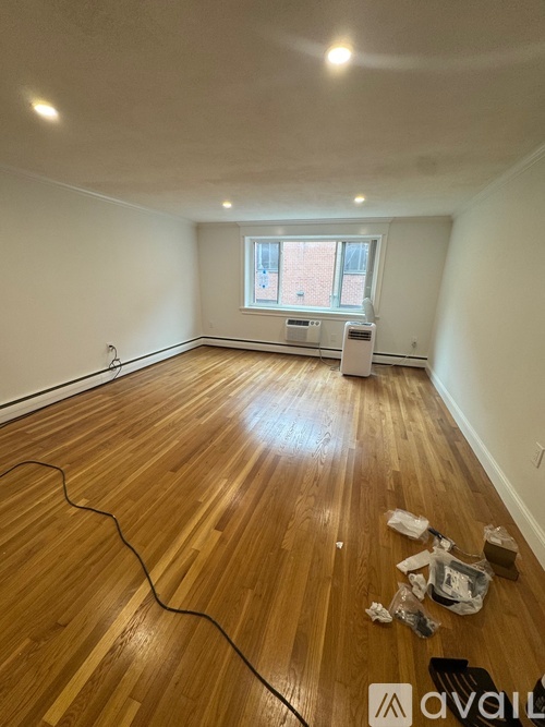 A room with wooden flooring and a window with a white radiator beneath it.