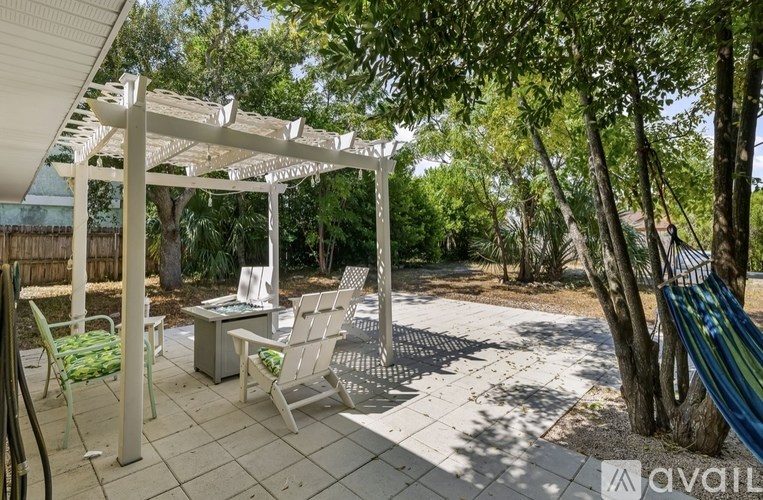 A patio with a white pergola and chairs.