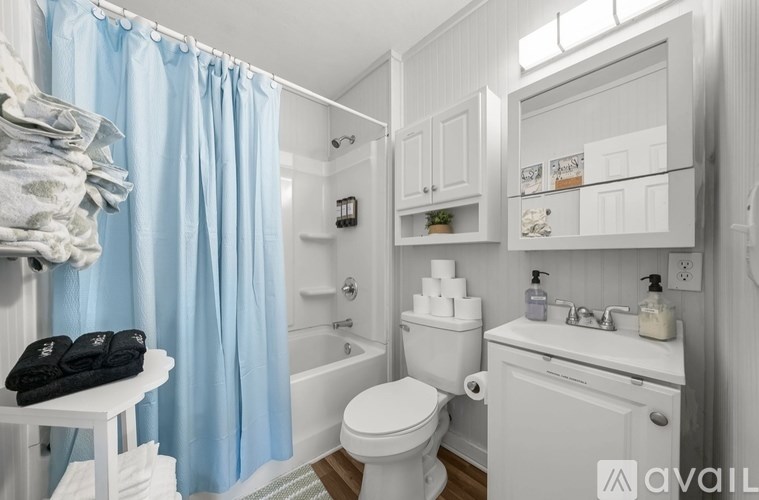 A bathroom with a white toilet, sink, and bathtub with blue curtains.