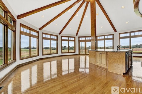 A spacious room with wooden floors and a large window overlooking a field.
