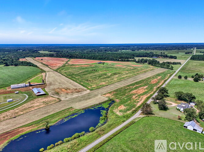 A large open field with a small lake and a few buildings.