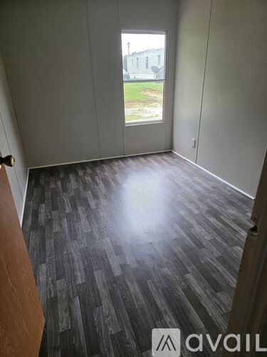 A room with a wooden floor and a window overlooking a green lawn.