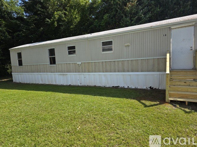 A long white building with a door and windows is surrounded by grass.