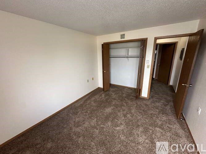 A carpeted room with a door on the right and a window with blinds on the left.