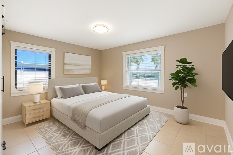 A bedroom with a large bed, a nightstand with a lamp, and a potted plant.