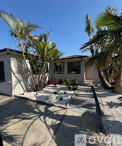 A white house with a driveway and palm trees in front.
