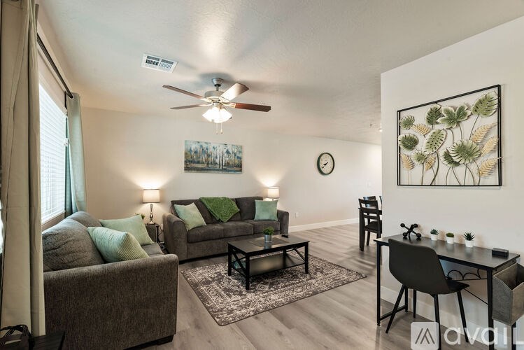 A living room with a grey couch, a black chair, a coffee table, and a ceiling fan.