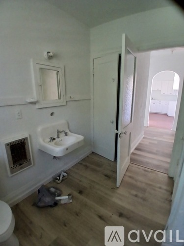 A bathroom with a toilet, sink, mirror, and a bag on the floor.