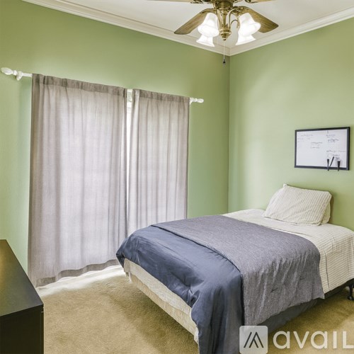 A bedroom with a bed, a ceiling fan, and a window with curtains.