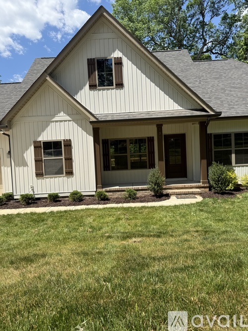 A two-story house with a garage is surrounded by trees and has a driveway leading to the garage.