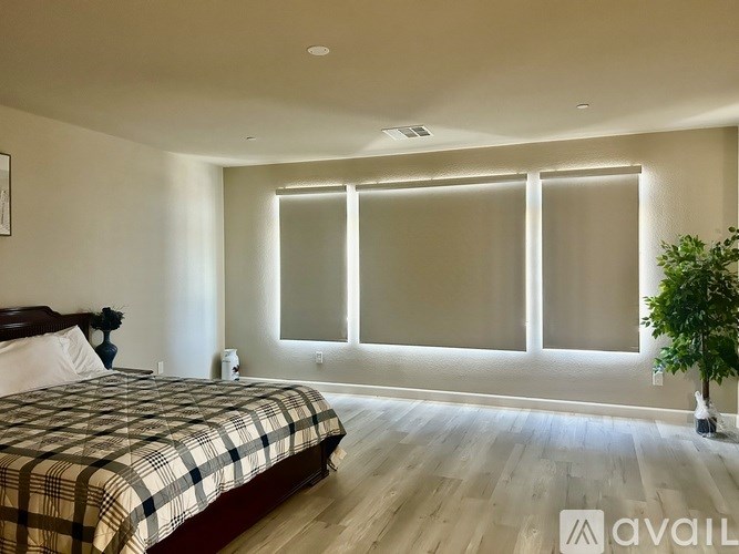 A bedroom with a bed, a plant, and a window with blinds.