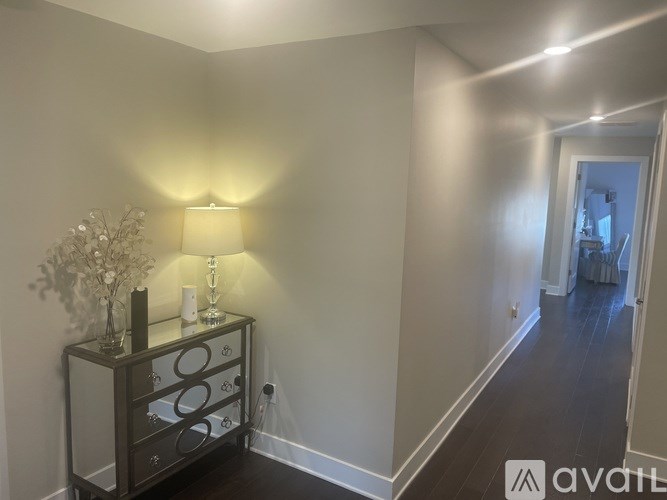 A hallway with a lamp and a vase of flowers on a cabinet.