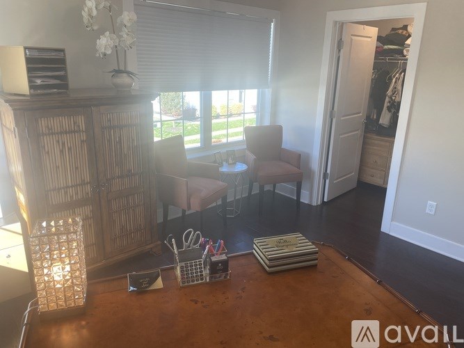 A room with a wooden floor, a chair, a table with a book and a vase with flowers on it.