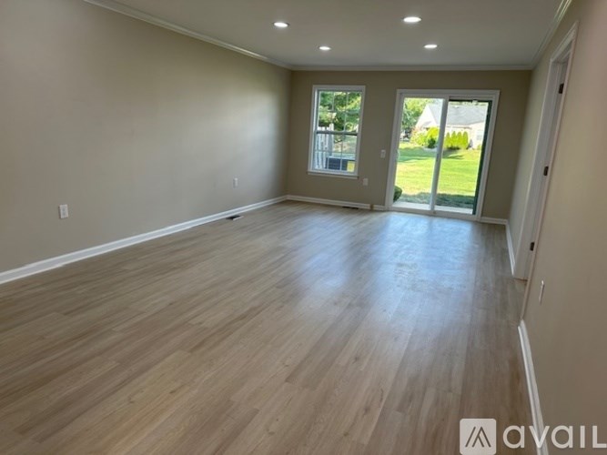 A spacious room with wooden flooring and a sliding glass door leading to a backyard.