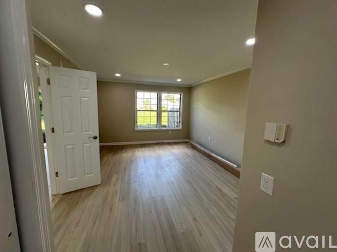 A room with a white door and a window with a view of a green lawn.